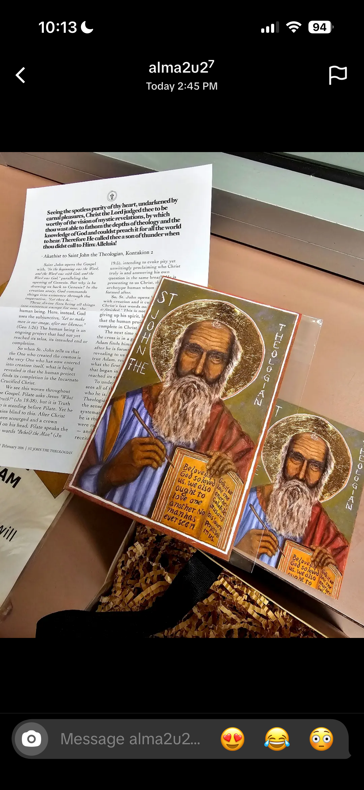 A close-up of a saint john the theologian icons with halos and gold ornamental borders, placed on top of printed prayer sheets on a desk.
