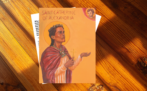 A religious art print or icon card titled 'Saint Catherine of Alexandria' featuring an illustration of the saint in a red robe and gold halo, placed on a wooden surface.